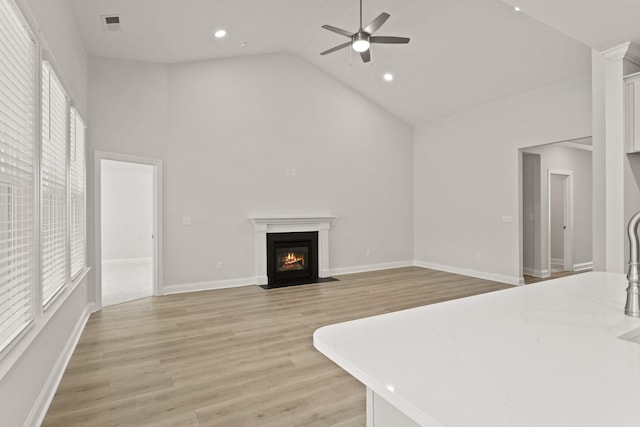 unfurnished living room featuring ceiling fan, a fireplace with flush hearth, a healthy amount of sunlight, and high vaulted ceiling