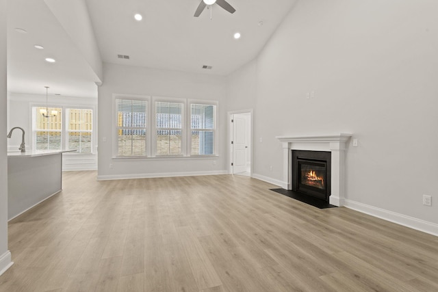 unfurnished living room with ceiling fan with notable chandelier, high vaulted ceiling, a fireplace with flush hearth, light wood-type flooring, and visible vents