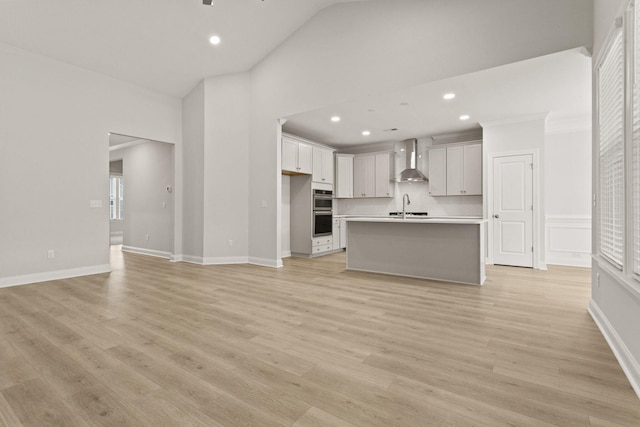 unfurnished living room with recessed lighting, light wood-style flooring, a sink, and high vaulted ceiling