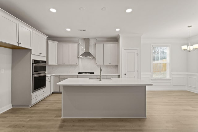 kitchen featuring a sink, wall chimney range hood, stainless steel double oven, light countertops, and black stovetop