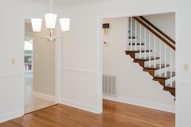 stairs with hardwood / wood-style floors, crown molding, and an inviting chandelier