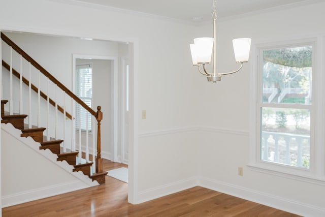 unfurnished dining area with hardwood / wood-style floors, crown molding, and a notable chandelier