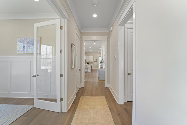 hall with wood finished floors, a wainscoted wall, recessed lighting, ornamental molding, and a decorative wall