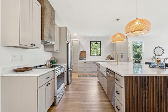 kitchen with light stone countertops, stainless steel appliances, pendant lighting, a large island with sink, and light hardwood / wood-style flooring