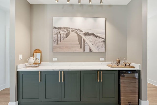 bar with light hardwood / wood-style floors, green cabinets, light stone countertops, and wine cooler