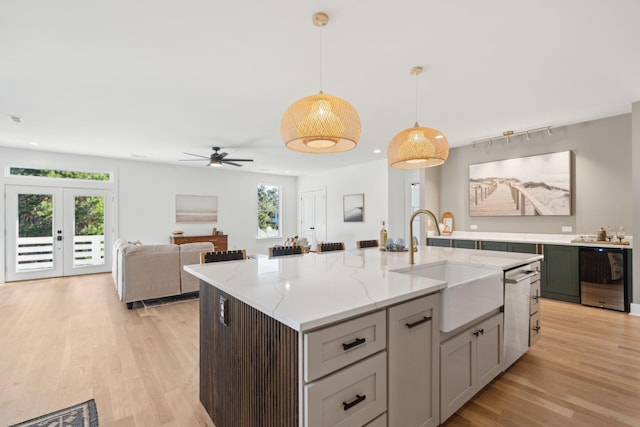 kitchen featuring french doors, ceiling fan, sink, a center island with sink, and hanging light fixtures