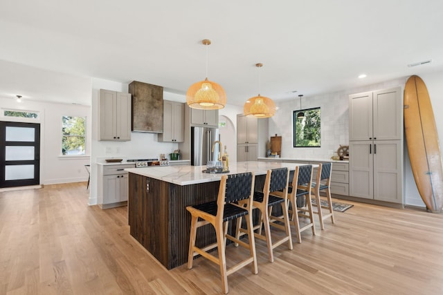 kitchen with decorative light fixtures, stainless steel fridge, light stone counters, a large island, and a kitchen bar