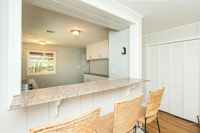 kitchen featuring a kitchen bar, kitchen peninsula, white cabinetry, and light hardwood / wood-style floors