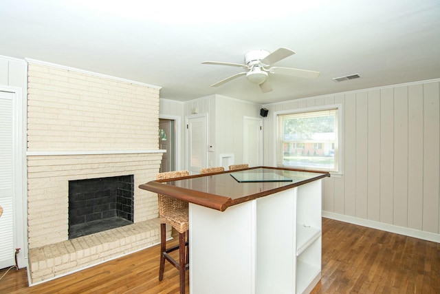 kitchen with dark hardwood / wood-style flooring, ceiling fan, crown molding, a fireplace, and a breakfast bar area