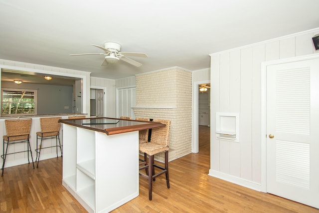 kitchen with ceiling fan, a kitchen bar, and wood-type flooring