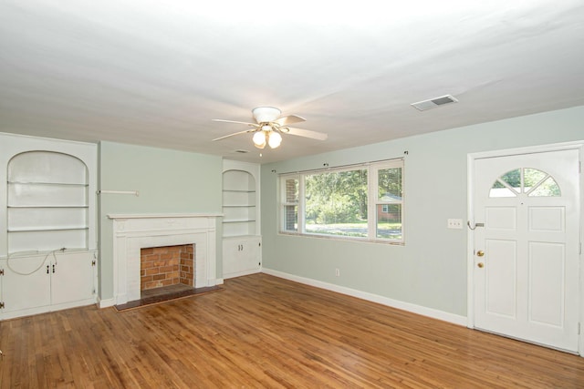 unfurnished living room featuring plenty of natural light, ceiling fan, wood-type flooring, and built in shelves