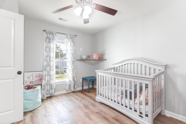 bedroom featuring ceiling fan, light hardwood / wood-style floors, and a nursery area