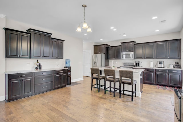 kitchen with appliances with stainless steel finishes, pendant lighting, a center island, light wood-type flooring, and a breakfast bar