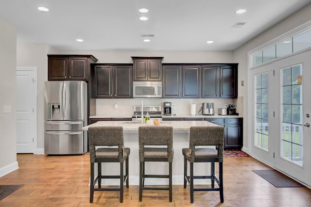 kitchen with tasteful backsplash, stainless steel appliances, light hardwood / wood-style floors, and a center island with sink