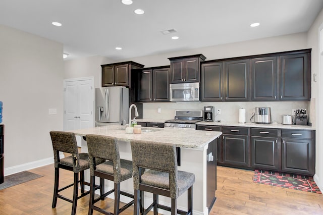 kitchen featuring dark brown cabinets, appliances with stainless steel finishes, a center island with sink, light wood-type flooring, and a breakfast bar