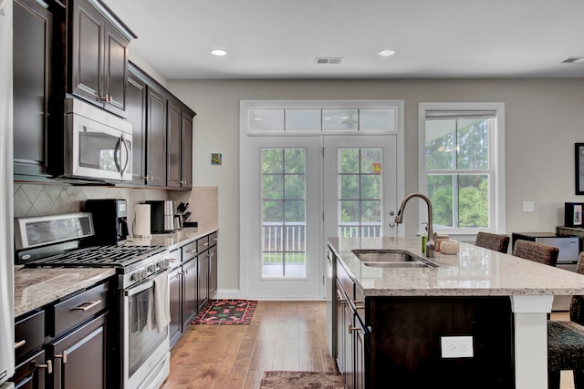 kitchen with appliances with stainless steel finishes, sink, backsplash, dark brown cabinets, and light hardwood / wood-style flooring