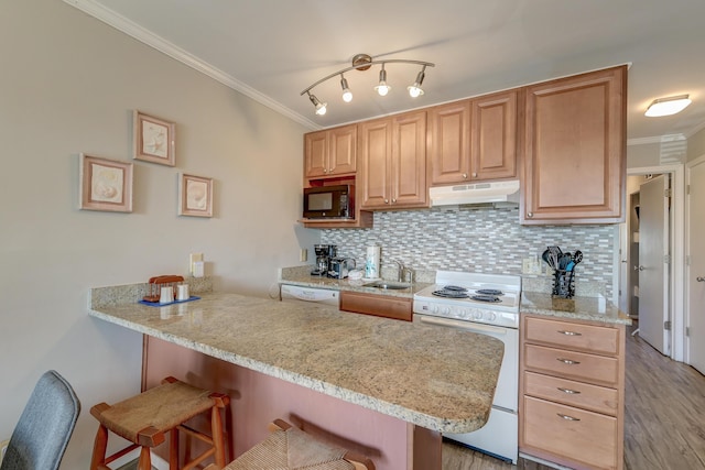 kitchen featuring under cabinet range hood, a kitchen bar, white appliances, and ornamental molding