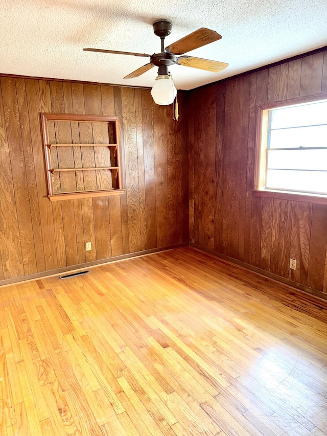 empty room featuring wood walls, hardwood / wood-style flooring, ceiling fan, and a textured ceiling