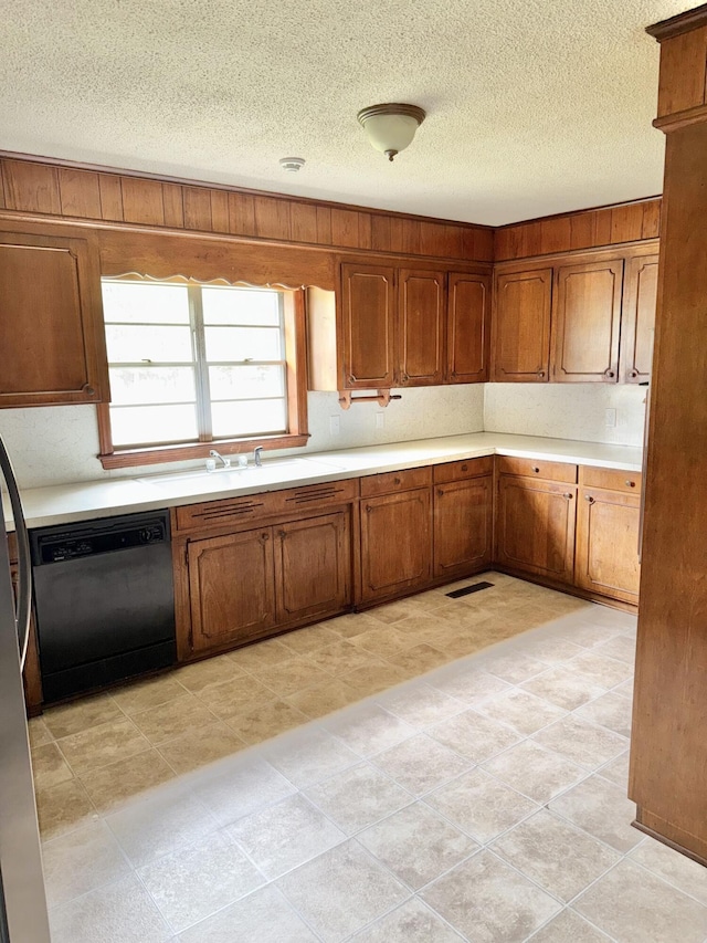 kitchen featuring brown cabinets, black dishwasher, light countertops, and a sink