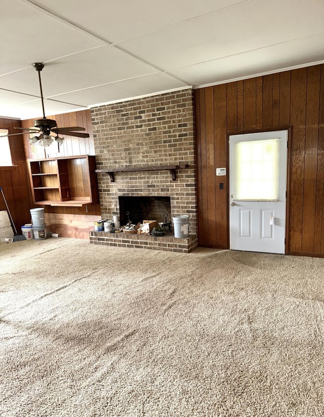 unfurnished living room with wood walls, carpet, ceiling fan, and a brick fireplace