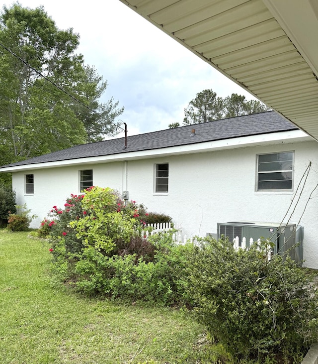 rear view of house featuring central AC, a shingled roof, stucco siding, and a lawn