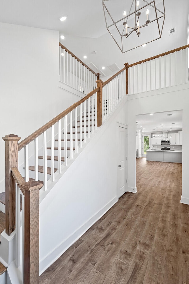 staircase featuring a towering ceiling, wood-type flooring, and an inviting chandelier