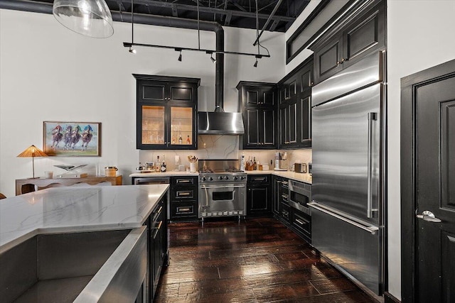 kitchen with built in appliances, light stone countertops, dark wood finished floors, and dark cabinetry
