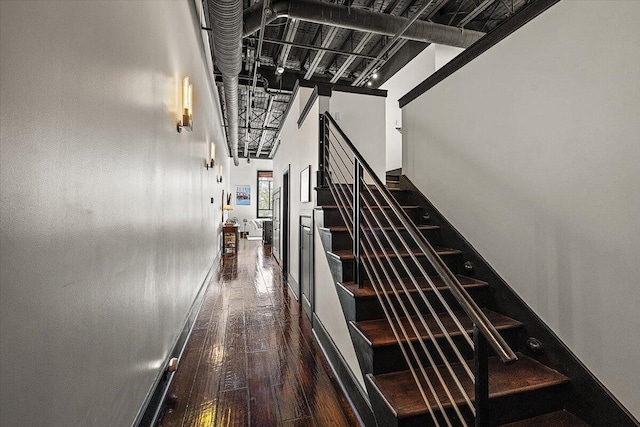 stairway featuring wood-type flooring, baseboards, and a high ceiling