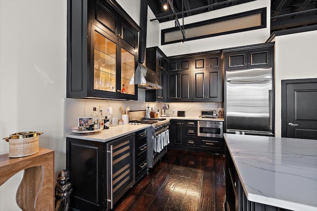 kitchen with dark wood-style flooring, light stone countertops, dark cabinets, beverage cooler, and premium appliances
