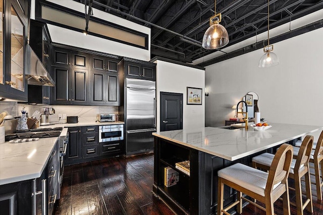 kitchen with dark cabinetry, dark wood-style flooring, built in refrigerator, and a sink