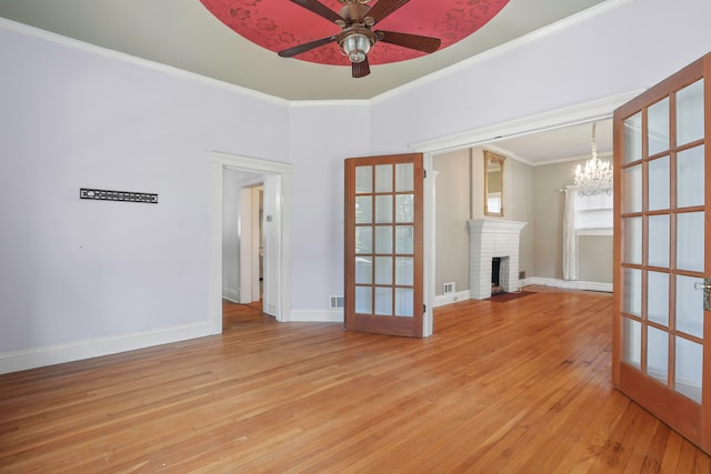 spare room featuring french doors, ornamental molding, hardwood / wood-style floors, a fireplace, and ceiling fan with notable chandelier