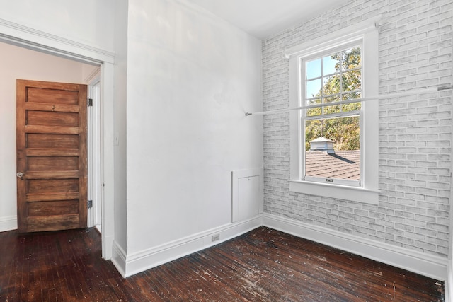 spare room featuring brick wall and dark hardwood / wood-style flooring