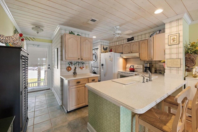 kitchen featuring ceiling fan, white appliances, backsplash, a kitchen breakfast bar, and stacked washer / dryer