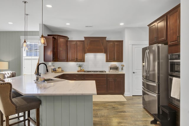 kitchen featuring sink, decorative light fixtures, light hardwood / wood-style floors, premium range hood, and appliances with stainless steel finishes