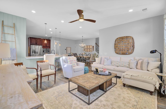 living room featuring ceiling fan with notable chandelier and light hardwood / wood-style flooring