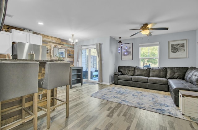 living room with light wood-type flooring, ceiling fan with notable chandelier, and wood walls