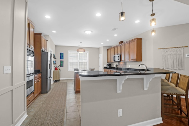 kitchen featuring appliances with stainless steel finishes, brown cabinets, a kitchen bar, a peninsula, and hanging light fixtures