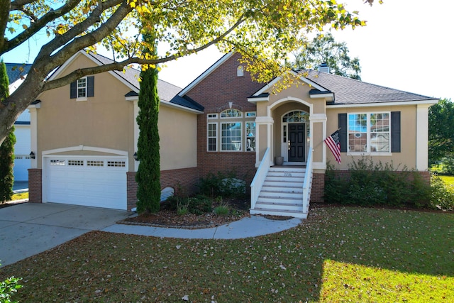 view of front facade featuring brick siding, a front lawn, driveway, stucco siding, and a shingled roof