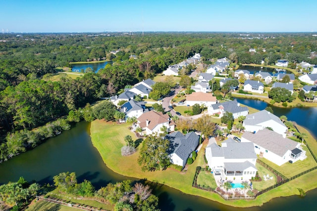 view of property location with a large body of water, nearby suburban area, and a heavily wooded area