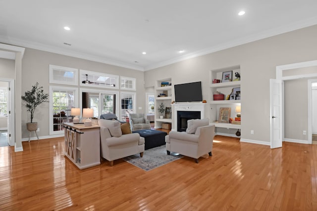 living area with light wood-type flooring, ornamental molding, recessed lighting, built in shelves, and baseboards