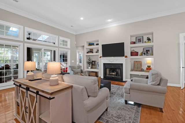 living room featuring crown molding, built in shelves, light wood-style flooring, a fireplace, and recessed lighting