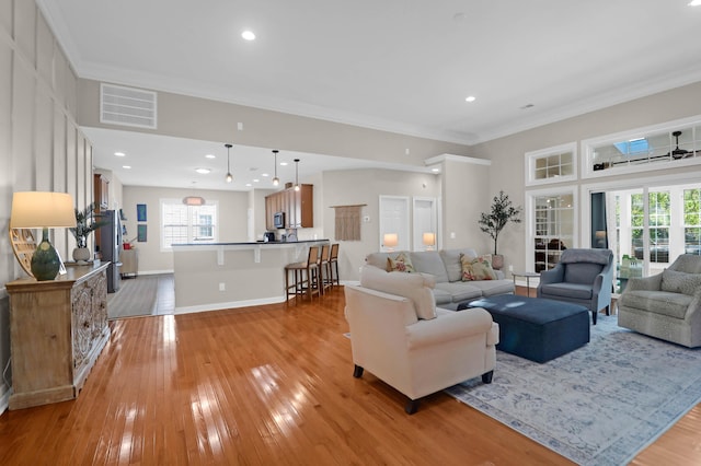living room featuring light wood-type flooring, crown molding, plenty of natural light, and baseboards
