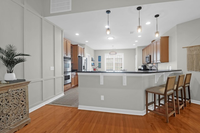 kitchen featuring appliances with stainless steel finishes, dark countertops, light wood finished floors, a peninsula, and recessed lighting
