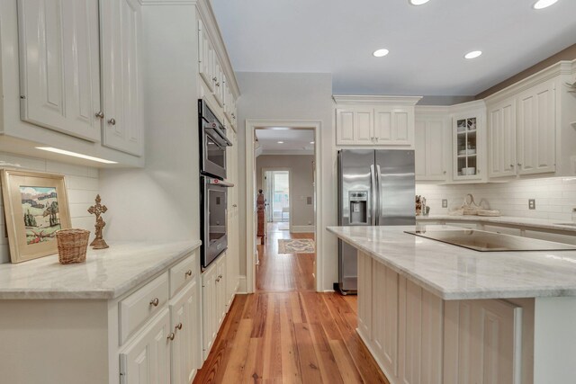 kitchen featuring crown molding, white cabinets, light hardwood / wood-style floors, light stone countertops, and stainless steel double oven