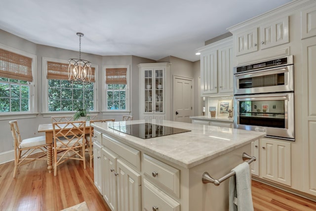 kitchen featuring decorative light fixtures, light wood-type flooring, black electric cooktop, a notable chandelier, and double oven