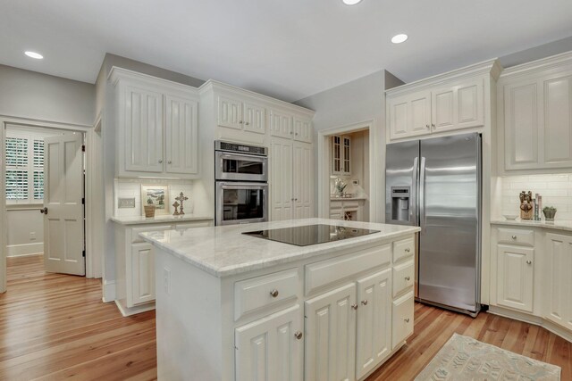 kitchen with a kitchen island, decorative backsplash, light wood-type flooring, and black appliances