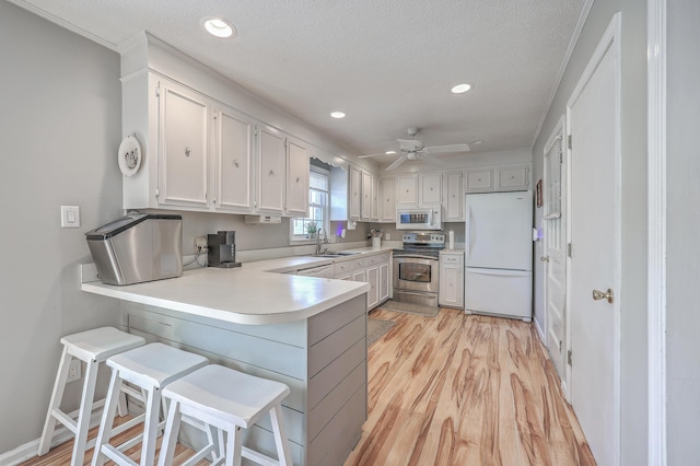 kitchen featuring a peninsula, white appliances, white cabinets, light countertops, and light wood-type flooring