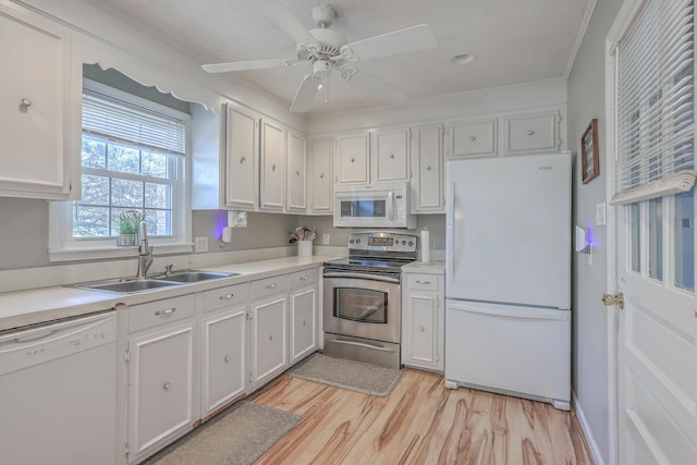 kitchen with white appliances, white cabinets, light countertops, light wood-type flooring, and a sink