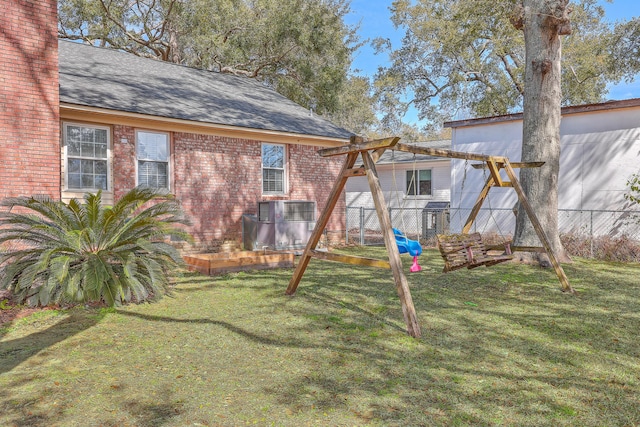 back of property with a yard, brick siding, a shingled roof, and fence