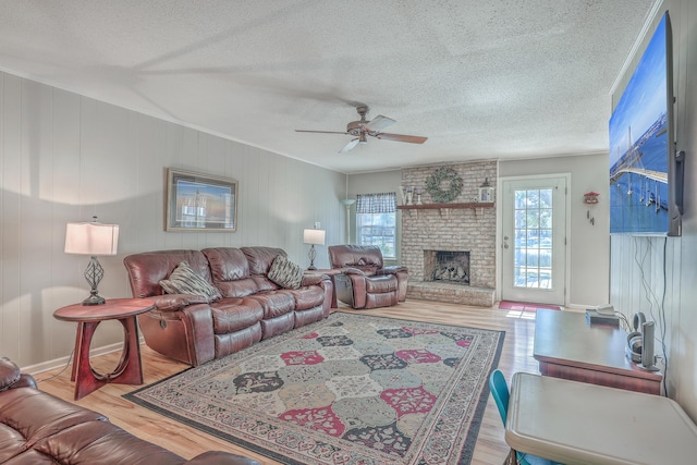 living room with a ceiling fan, a fireplace, a textured ceiling, and wood finished floors